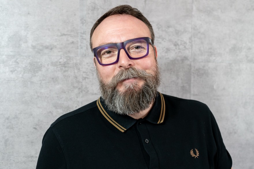 Retrato de estudio de Pedro Bisbal en color, sonriente, con gafas y barba