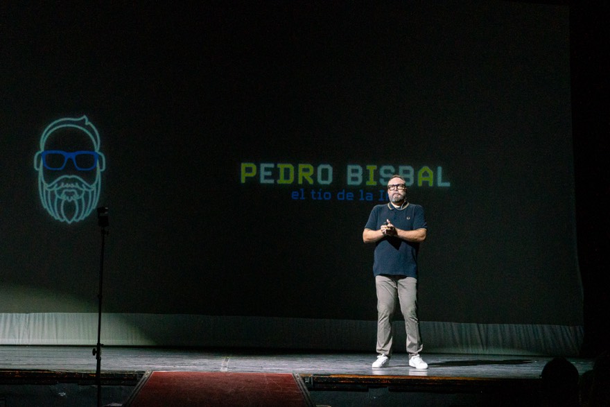 Pedro Bisbal en un teatro a oscuras con su logo neón y el rótulo «el tío de la IA» proyectados en pantalla
